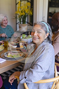 Happy biracial senior woman celebrating with friends at christmas dinner in sunny dining room