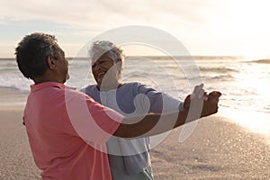 Happy biracial senior woman enjoying romantic dance with man at beach during sunset