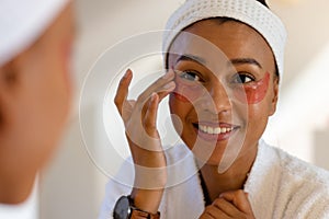 Happy biracial woman in bathrobe wearing eye mask in bathroom