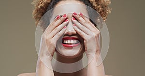 Happy biracial woman with dark hair and red lips and nails on beige background, slow motion