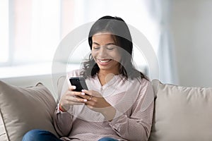 Happy biracial woman relax on sofa using smartphone