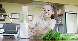 Happy biracial woman using blender, preparing smoothie in kitchen