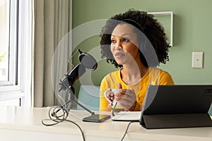 Happy biracial woman using headphones, tablet and microphone podcasting from home