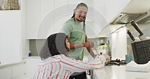 Happy biracial woman in wheelchair talking with smiling male partner preparing food in kitchen