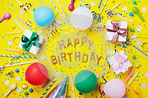 Happy birthday background or greeting flyer. Colorful holiday supplies on yellow table top view. Flat lay style.