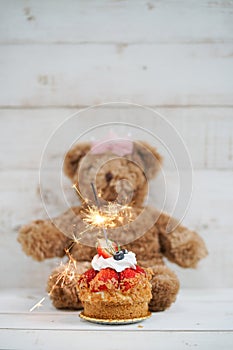 Happy Birthday. Birthday cake with blurred teddy bear on the white wooden background. Soft focus on strawberry. photo