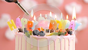 Happy Birthday Candle Cake on pink background. Every candle is lit by lighter. Close-up