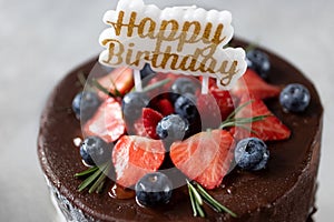 Happy Birthday candles on chocolate cake with strawberry and blueberry