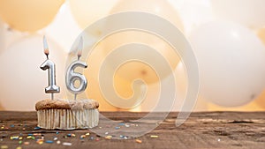 Happy birthday card with candle number 16 in a cupcake against the background of balloons. Copy space happy birthday for sixteen