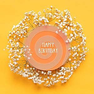 Happy Birthday Card. Flat lay greeting card with beautiful little white flowers on bright yellow paper background.