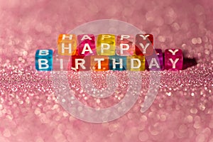 Happy Birthday with colored blocks letters on pink glitter backgrounds. Postcard to celebrate. Copy space