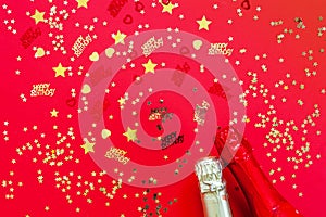 Happy birthday concept with golden glitter confetti and shampagne bottles  on the red background