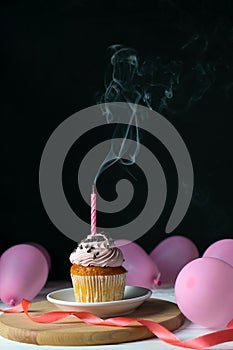 Happy birthday cupcake with a candle blown out on a black background with balloons