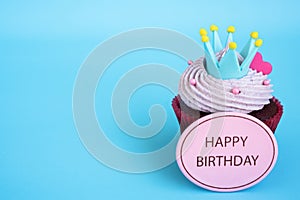 Happy birthday cupcake with crown and pink heart over blue background