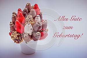 Happy birthday greeting card in German that reads Alles Gute zum Geburtstag with red lettering; A bundle of edible flowers,