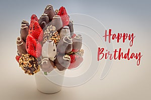 Happy birthday greeting card with red brush lettering; A bundle of edible flowers, arrangement of strawberries covered with