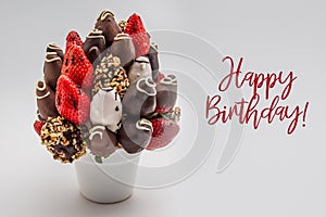 Happy birthday greeting card with red brush lettering; A bundle of edible flowers, arrangement of strawberries covered with