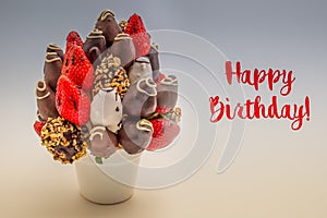 Happy birthday greeting card with red lettering; A bundle of edible flowers, arrangement of strawberries covered with chocolate