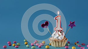 Happy birthday greetings to 1 year old baby, birthday cupcake with candles and birthday decorations on blue background