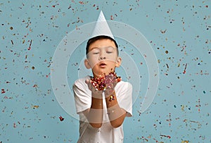 Happy Birthday. Little Asian Boy Wearing B-Day Hat Blowing Confetti At Camera