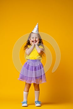 Happy Birthday! little girl in festive hat on her birthday on yellow background