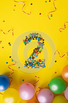 Happy Birthday number 2 made of candies with colorful balloons on yellow background