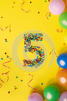 Happy Birthday number 5 made of candies with colorful balloons on yellow background