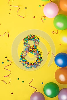 Happy Birthday number 8 made of candies with colorful balloons on yellow background