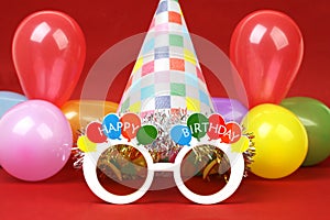 Happy birthday party glasses, party hat and party balloons on red background