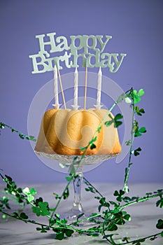 Happy birthday ring cake with clover decoration on marble table and lilac background