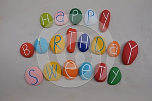 Happy Birthday Sweety with colored stones over white sand