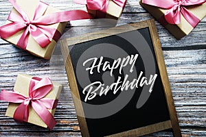 Happy Birthday text on blackboard with gift boxes on wooden background