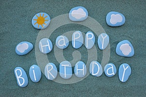 Happy Birthday text composed with blue colored stone letters over green sand