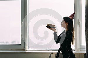 Happy birthday, woman holding cake looking at candle, window background, profile view