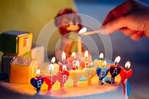 Happy Birthday Written In Lit Candles On Colorful Cake. Hand Holding A Wooden Match That Lighting