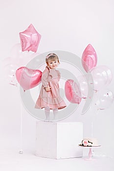 Happy birthday 2 years old little girl in pink dress. white cake with candles and roses. Birthday decorations with white and pink