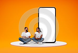 Happy Black Couple With Cellphones Sitting Near Bog Smartphone With Blank Screen