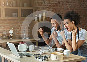 Happy black couple cooking pastry looking on laptop