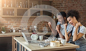 Happy black couple cooking pastry looking on laptop