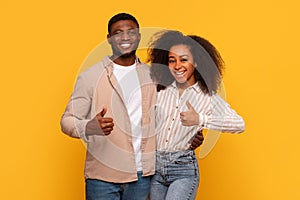 Happy black couple giving thumbs up, vibrant yellow background