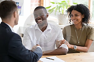 Happy black couple handshaking realtor insurer landlord at meeting