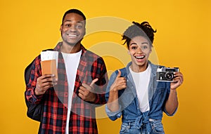 Happy Black Couple Holding Camera And Travel Tickets, Yellow Background