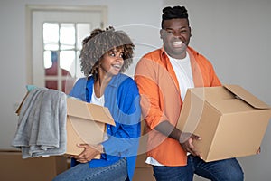 Happy black couple holding carton boxes and walking in their new apartment