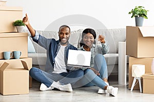 Happy Black Couple Holding Home Keys And Demonstrating Laptop With Blank Screen