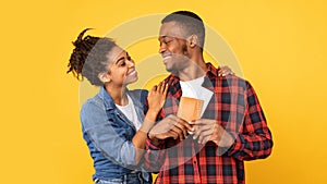 Happy Black Couple Hugging Holding Flight Tickets Over Yellow Background