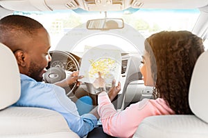 Happy black couple looking at map sitting inside car