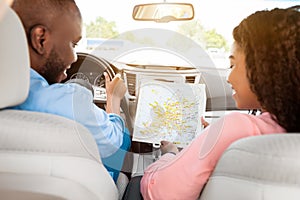 Happy black couple looking at paper map sitting inside car