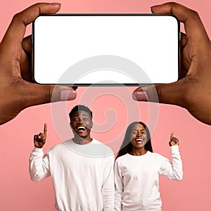 Happy Black Couple Pointing At Big Blank Smartphone In Giant Female Hands
