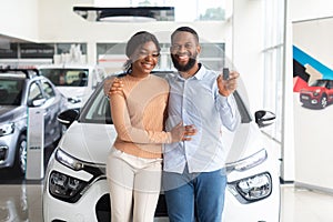 Happy Black Couple Posing With Car Keys In Hands In Dealership Center