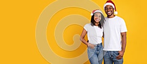 Happy Black Couple In Santa Hats Embracing Over Yellow Background